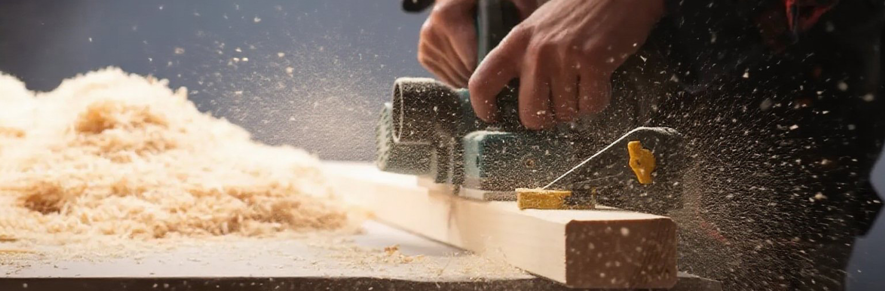 A worker carefully planing a wooden beam in a furniture factory workshop.